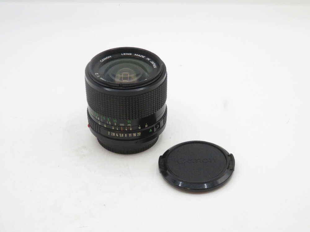 IMG_1421 A Canon camera lens with a textured grip, displayed next to its detached lens cap on a plain white background.