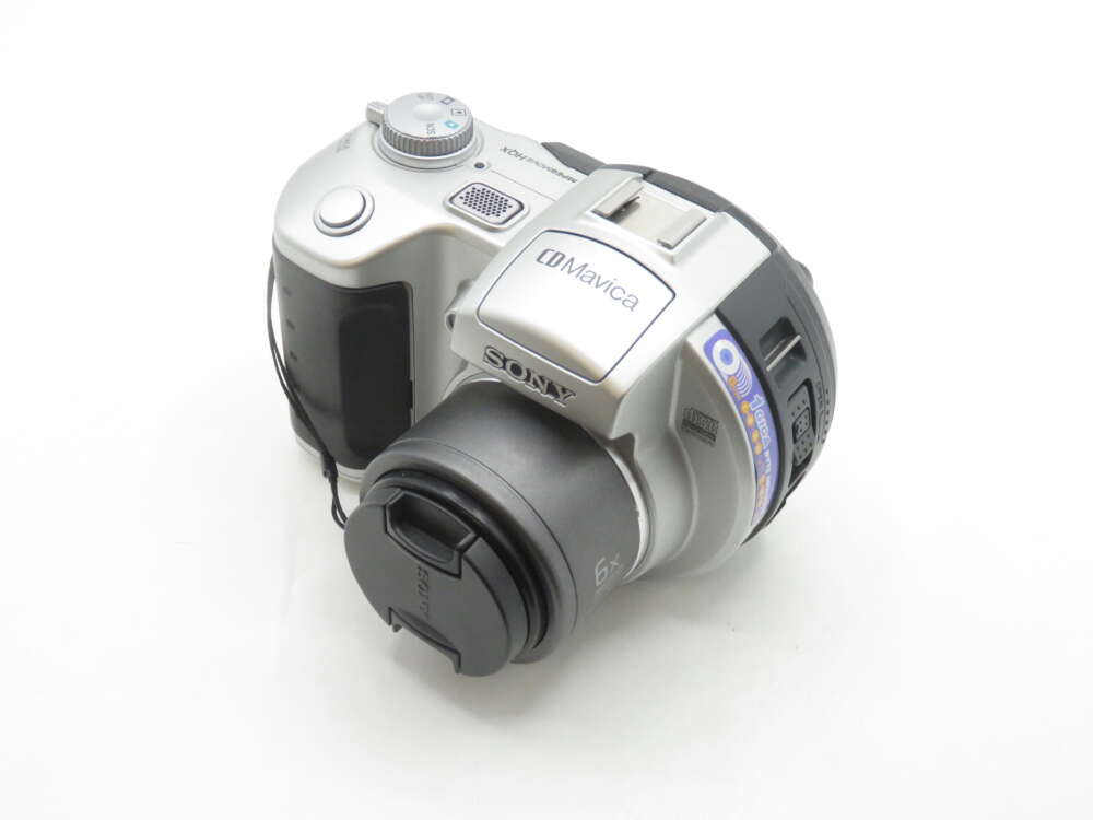 IMG_1452 A silver Sony CD Mavica digital camera with a lens cap, shown from a top-side angle with control dials and a carrying strap visible.