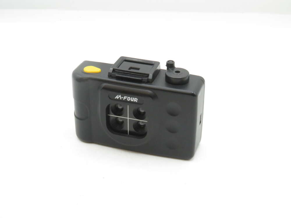 IMG_1481 A small black multi-lens camera with four lenses arranged in a square pattern, featuring a yellow shutter button on the top and the label 'M-Four' on the front.