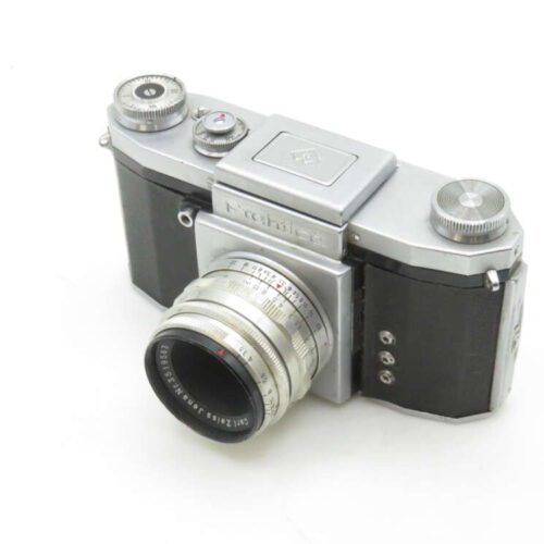 A vintage Praktica camera with a metallic body, featuring a Zeiss Jena lens and various dials on the top for settings.
