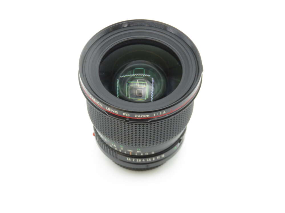 IMG_1602 A Canon 24mm f/1.4 FD lens with a prominent front glass element and a textured focus ring, viewed from above on a white background.