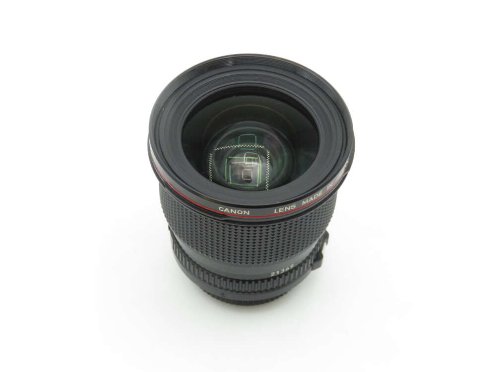 A Canon camera lens with a black body and textured grip, featuring a red ring near the top, viewed from above on a white background.