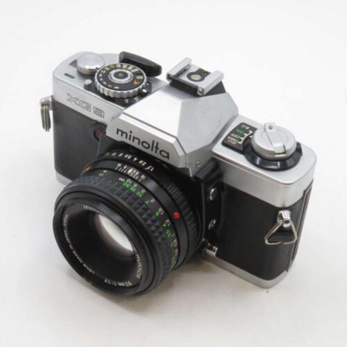 A vintage Minolta XG 9 film camera with a 50mm lens attached, featuring a silver body and black textured grip, placed on a plain white background.