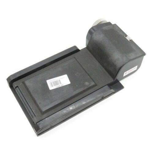A black electronic device with a rectangular base and rounded upper section containing a knob, possibly a specialized piece of industrial equipment. A white label with text and a barcode is attached to the top surface.