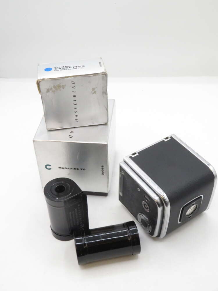 IMG_1687 A Hasselblad camera magazine with its original packaging, alongside two black film cassettes, arranged on a plain background.