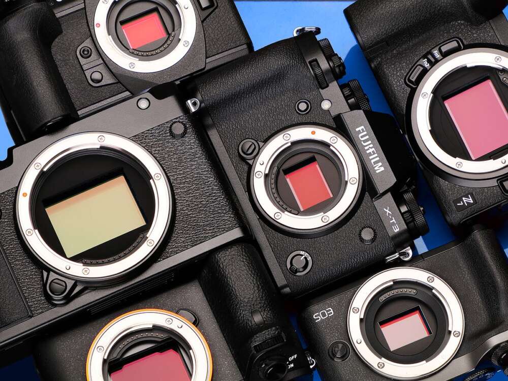 A collection of black digital cameras without lenses, showcasing the exposed sensors, arranged against a blue background.