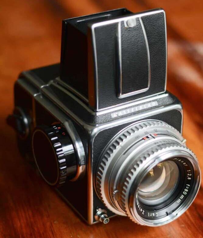 A vintage medium format camera with a black and silver body and a prominent lens sits on a wooden surface.