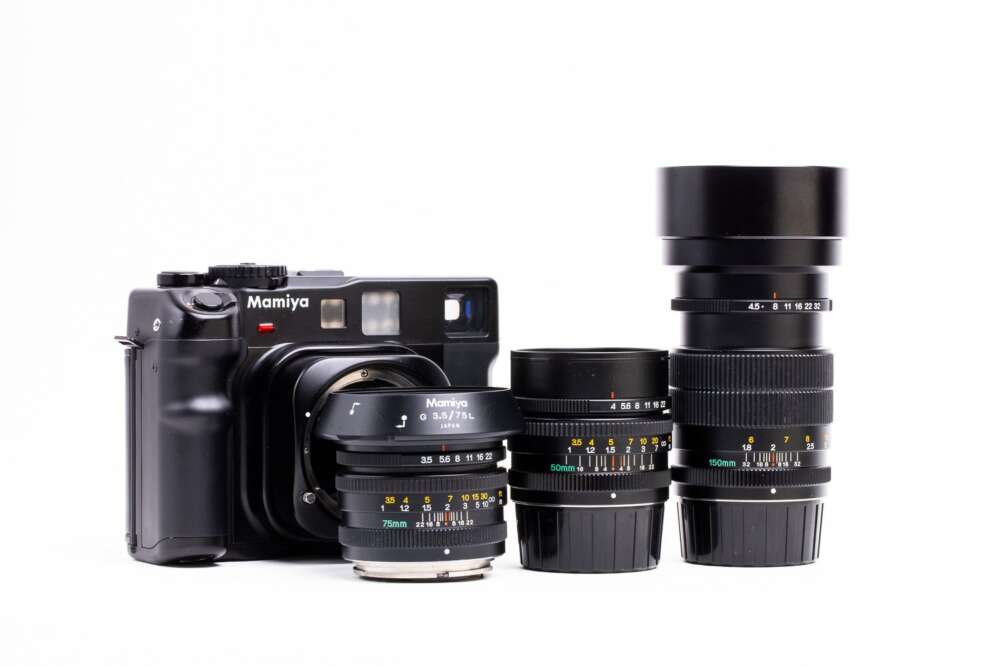 A Mamiya camera with three interchangeable lenses of different focal lengths set against a white background.