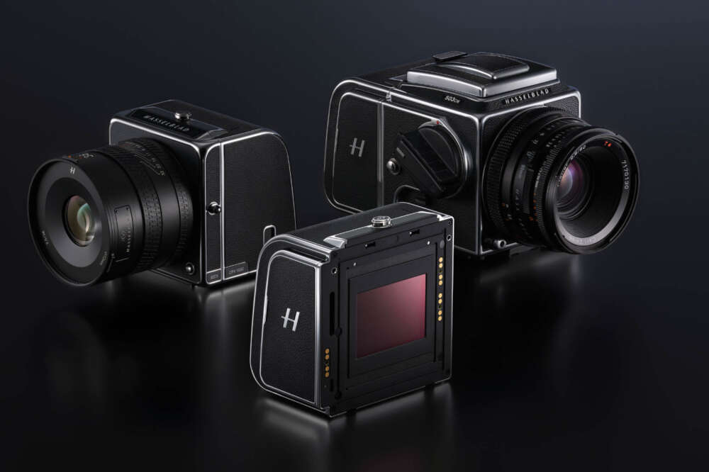 Three medium format cameras with black bodies and attached lenses displayed on a dark surface, showcasing a sleek, vintage design.