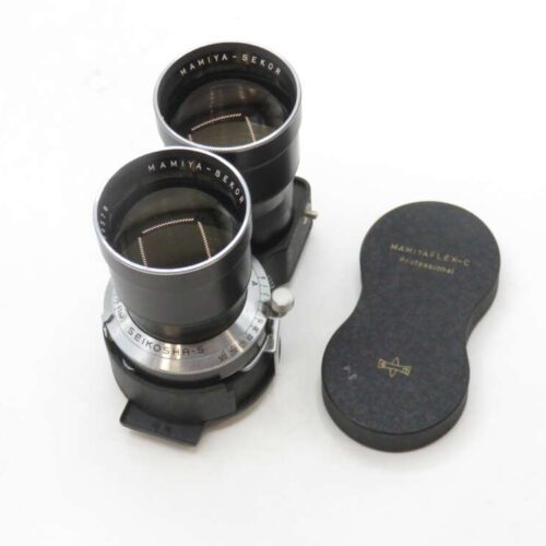 A vintage Mamiya-Sekor dual lens from a Mamiyaflex-C camera with its black protective cap beside it.