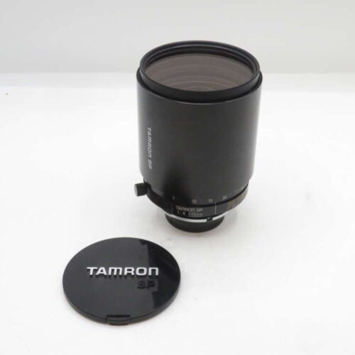 A Tamron SP camera lens with its detached front lens cap placed beside it, all set against a plain white background.