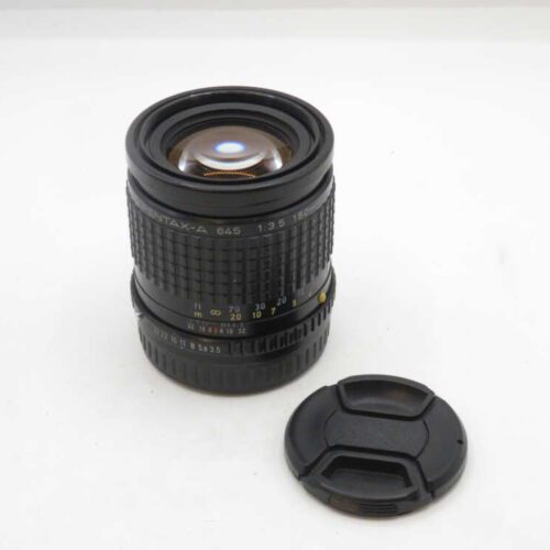 A Pentax-A 645 1:3.5 150mm camera lens with a black lens cap placed beside it on a white surface.