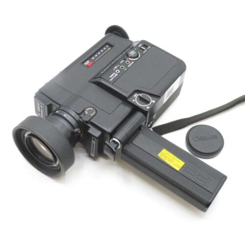 A vintage Canon video camera with a wide lens, side control panel, and carrying strap, placed on a white background beside a lens cap.