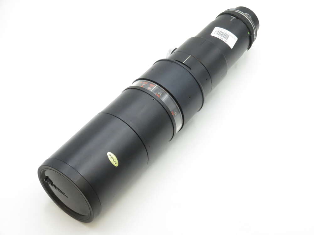 IMG_1901 A large, black telephoto camera lens with a zoom ring and distance scale, positioned on a white background.