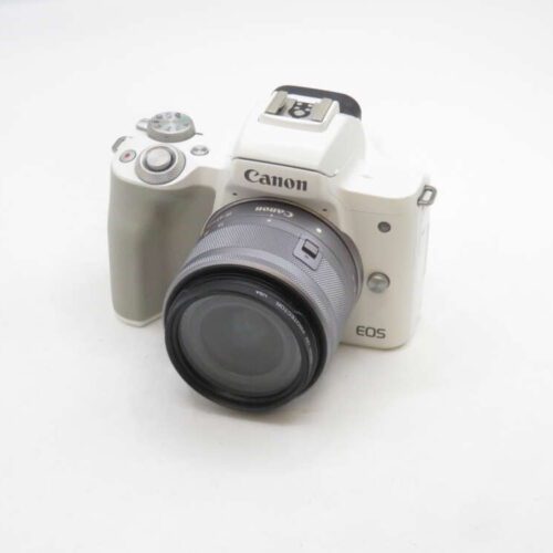 A white Canon EOS mirrorless camera with a zoom lens attached, placed on a plain white surface.