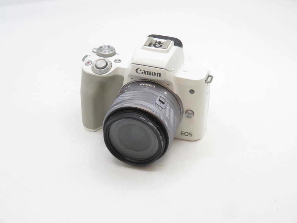 IMG_1941 A white Canon EOS mirrorless camera with a zoom lens attached, placed on a plain white surface.