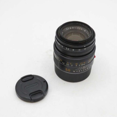A Leica Summicron-M 50mm f/2 lens with a black body and a detachable lens cap placed beside it, on a plain white background.