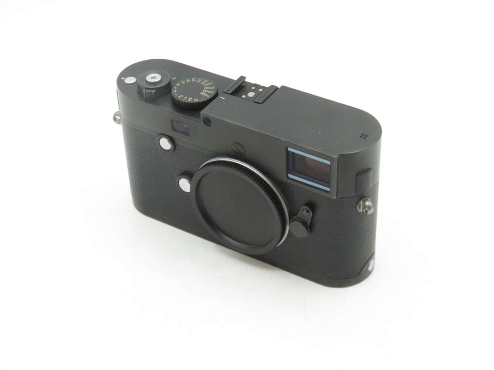 IMG_1967 A black rangefinder-style camera with a body cap on the lens mount, featuring a textured grip and various control dials on the top.