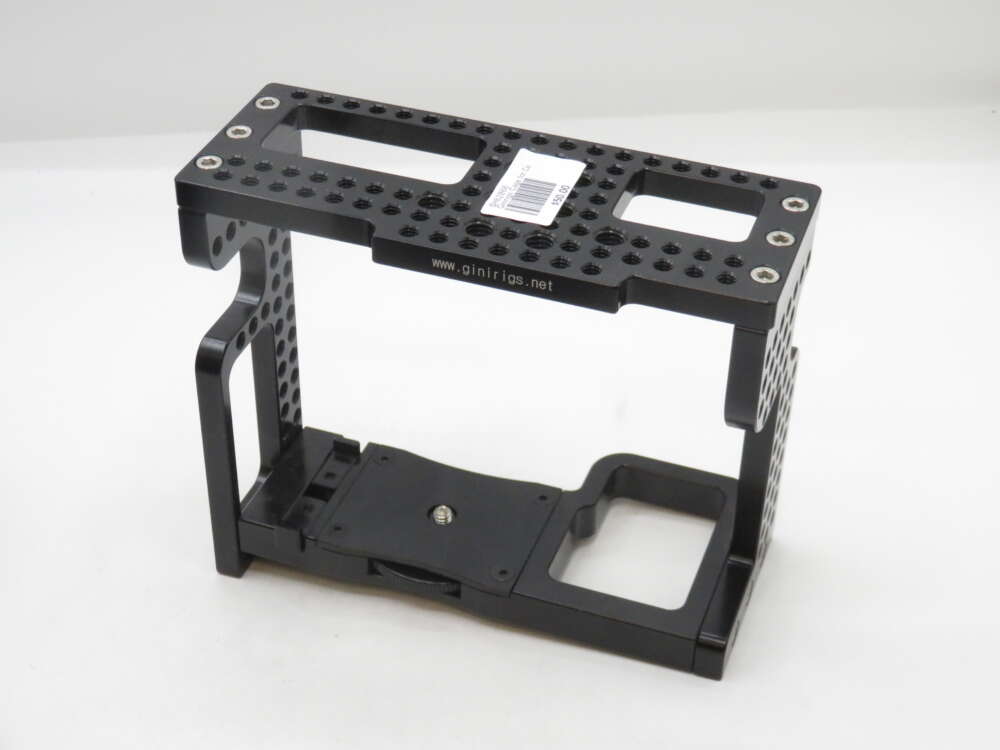 IMG_2011 A black metal camera cage with multiple mounting holes, designed to hold and protect a camera, placed on a plain background.