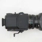 A top view of a black medium format film camera with a 75mm lens and a rectangular lens hood. The camera has a textured body and several control dials visible on the top panel.