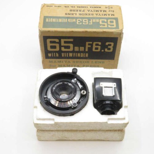 A Mamiya Sekor 65mm F6.3 lens with a viewfinder, alongside a cardboard box labeled "65mm F6.3 with Viewfinder Mamiya Sekor Lens for Mamiya Press." The items are displayed on white foam packaging.
