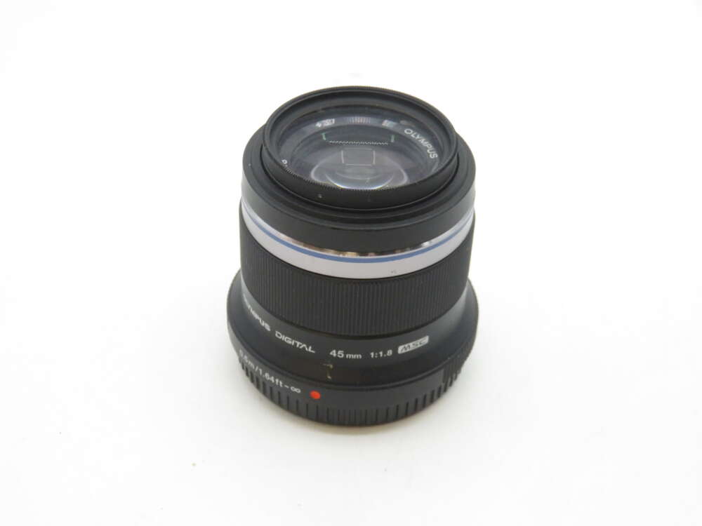 IMG_2155 A black Olympus 45mm f/1.8 digital camera lens with a textured focus ring, shown against a plain white background.
