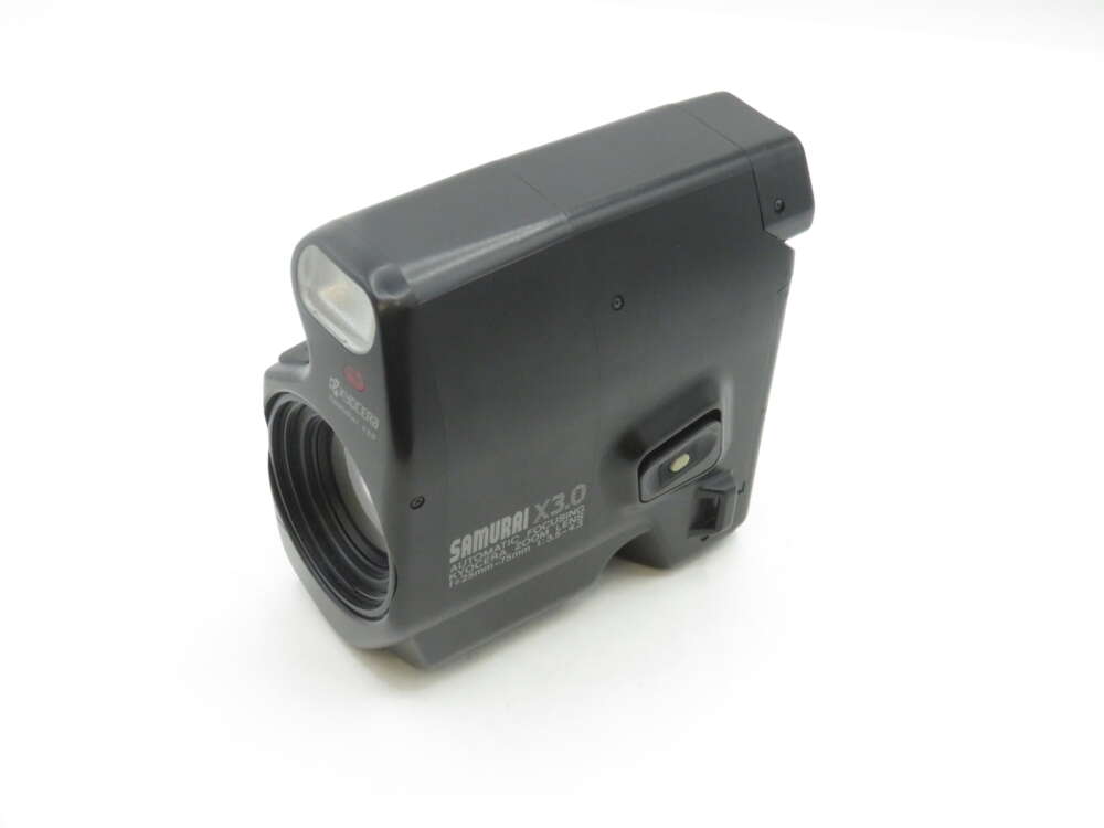 IMG_2202 A black Kyocera Samurai X3.0 camera with a unique vertical design and a prominent lens at the bottom left. The camera features branding and model information printed in white text on the side.