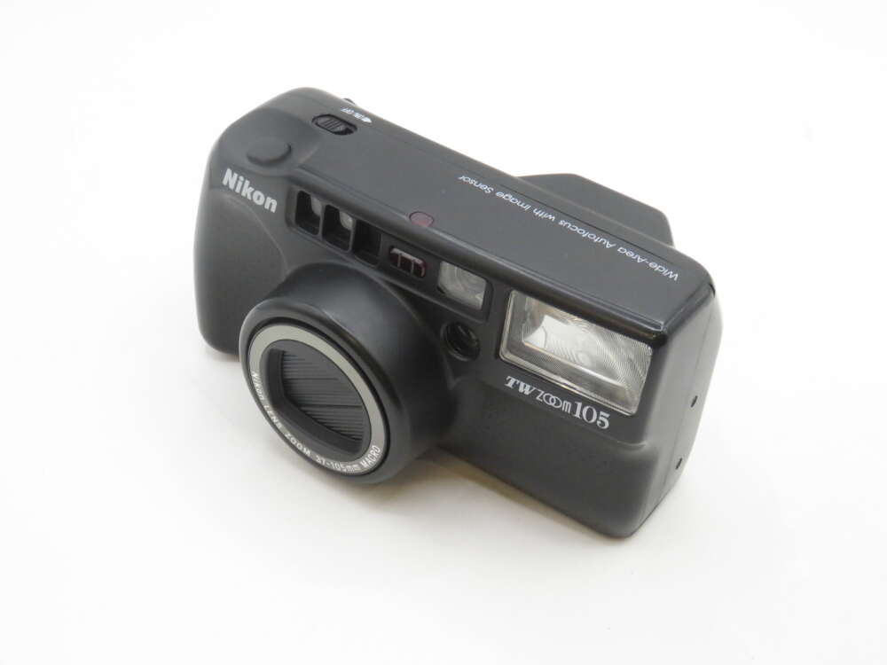IMG_2204 A black Nikon TW Zoom 105 film camera with a distinctive boxy design, featuring a protruding lens, viewfinder, and flash on the front, resting on a white surface.
