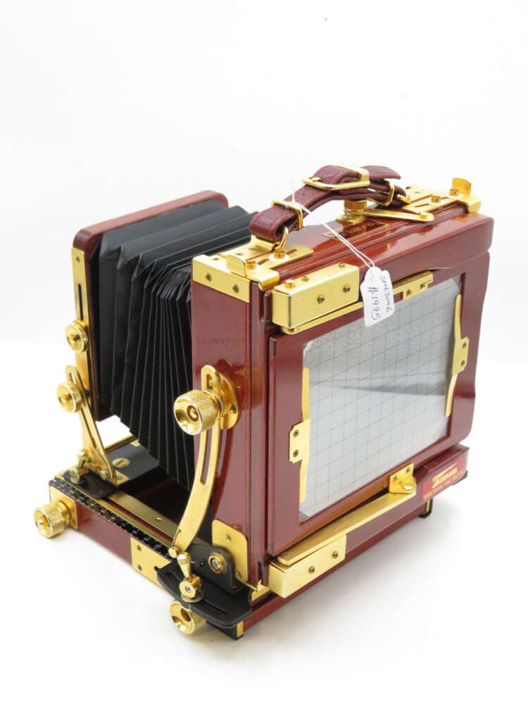 A vintage wooden large format camera with brass fittings and black bellows, showcasing intricate details and craftsmanship on a plain white background.
