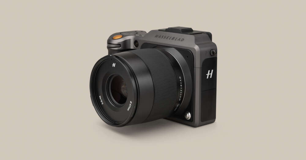 Camera with a lens attached, featuring the Hasselblad logo on the body, set against a plain beige background.