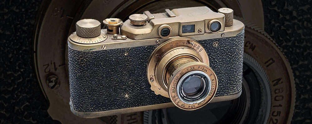 A vintage Leica film camera with a textured black body and brass detailing, set against an enlarged lens background.