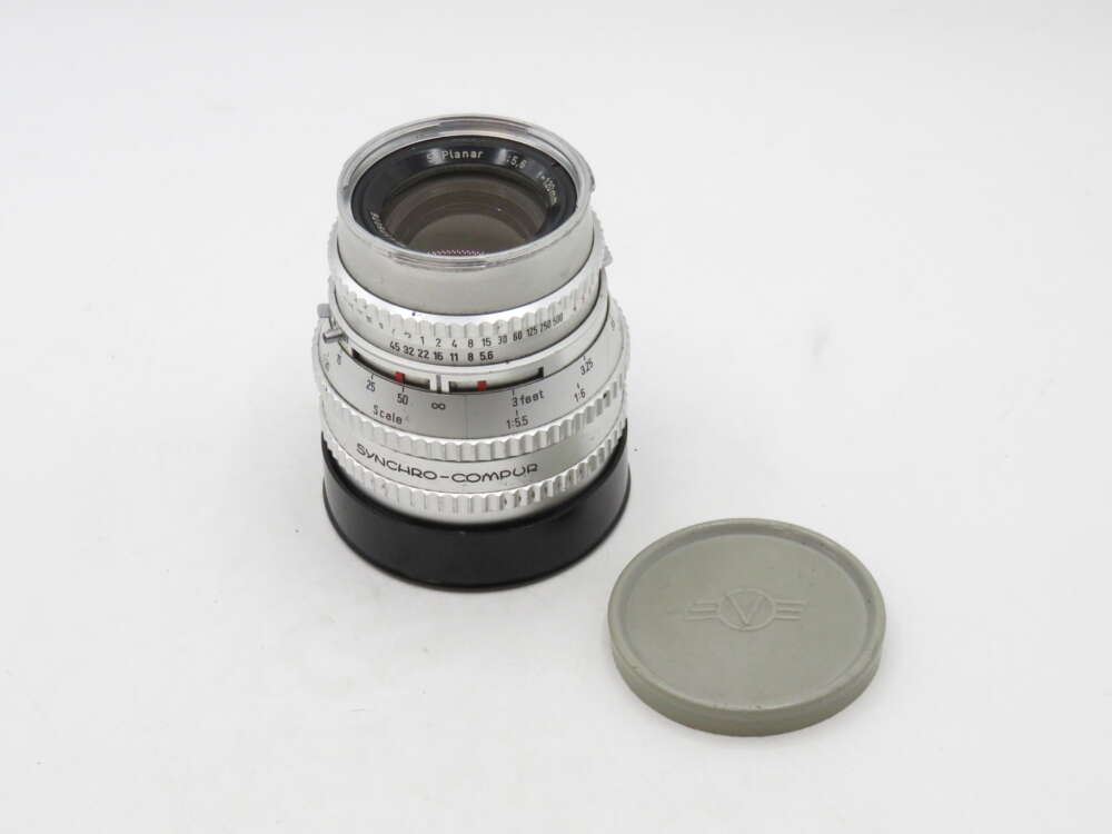 IMG_3074 A vintage camera lens with a silver exterior and various control rings is next to a grey lens cap.