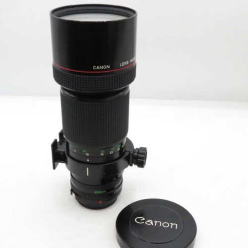 A Canon telephoto camera lens with a black body, adjustable zoom ring, and lens cap placed beside it.