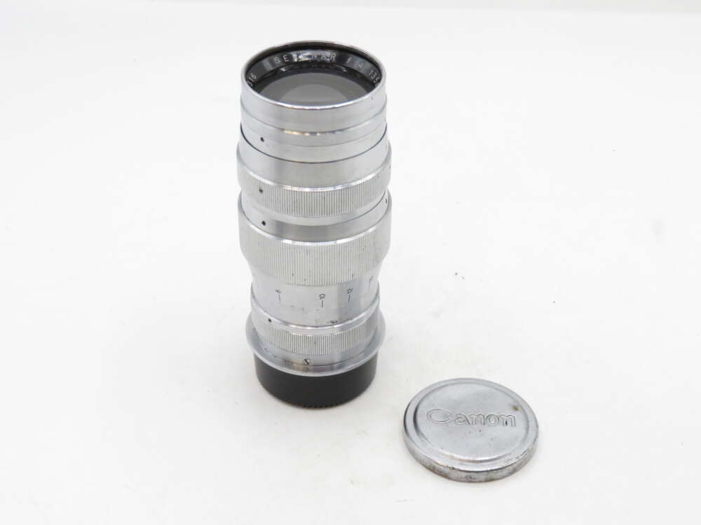 IMG_3118 A vintage silver camera lens with a black base beside a round lens cap with "Canon" text.