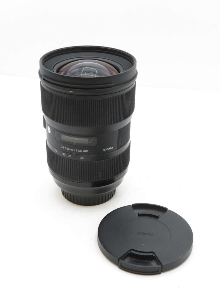 Camera lens with a wide aperture ring, labelled 'Sigma 24-35mm 1:2 DG HSM', next to a matching lens cap.