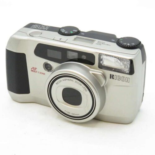 A silver Ricoh camera with a retractable lens and various buttons and dials on top.