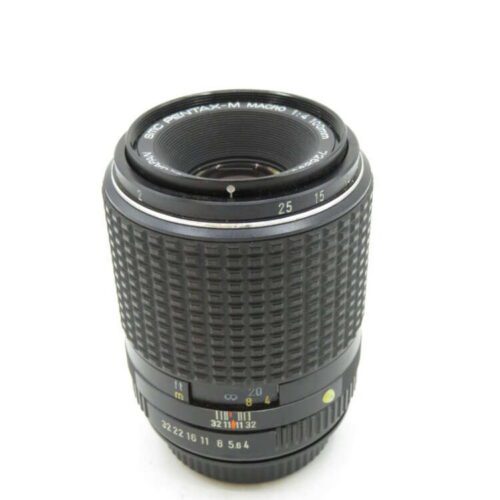A Pentax-M macro camera lens with distance markings and ribbed grip, standing upright on a white background.