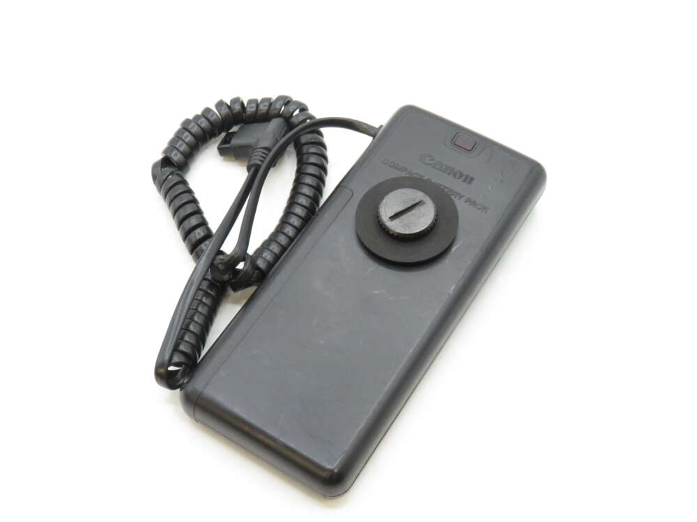 IMG_3355 A black Canon Compact Battery Pack with a coiled cord attached.