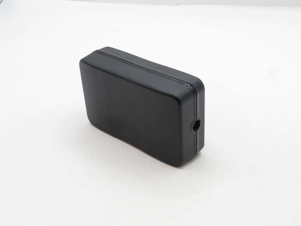 IMG_3356 A black rectangular plastic enclosure with a small hole on one side, set against a plain white background.