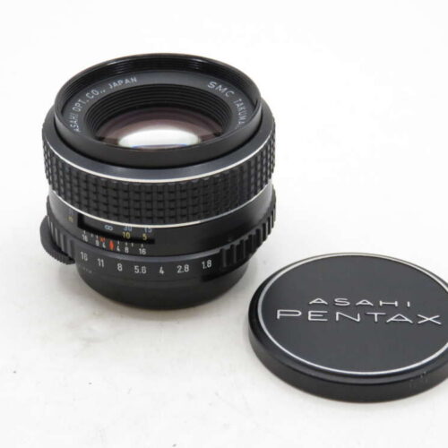 A vintage Asahi Pentax camera lens with its cap, featuring detailed aperture markings.