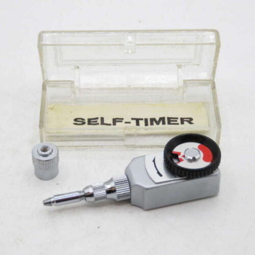 A mechanical self-timer device with a black and red dial, positioned next to a transparent case labeled "SELF-TIMER".