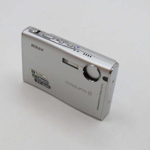 Silver Nikon Coolpix digital camera on a white surface, featuring a lens, flash, and various buttons on top.