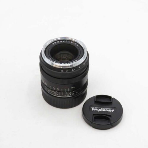 A Voigtländer camera lens with numerical markings and a matching lens cap on a plain white surface.