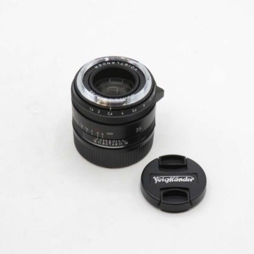 A Voigtländer camera lens with a 35mm marking, accompanied by its lens cap on a plain white background.