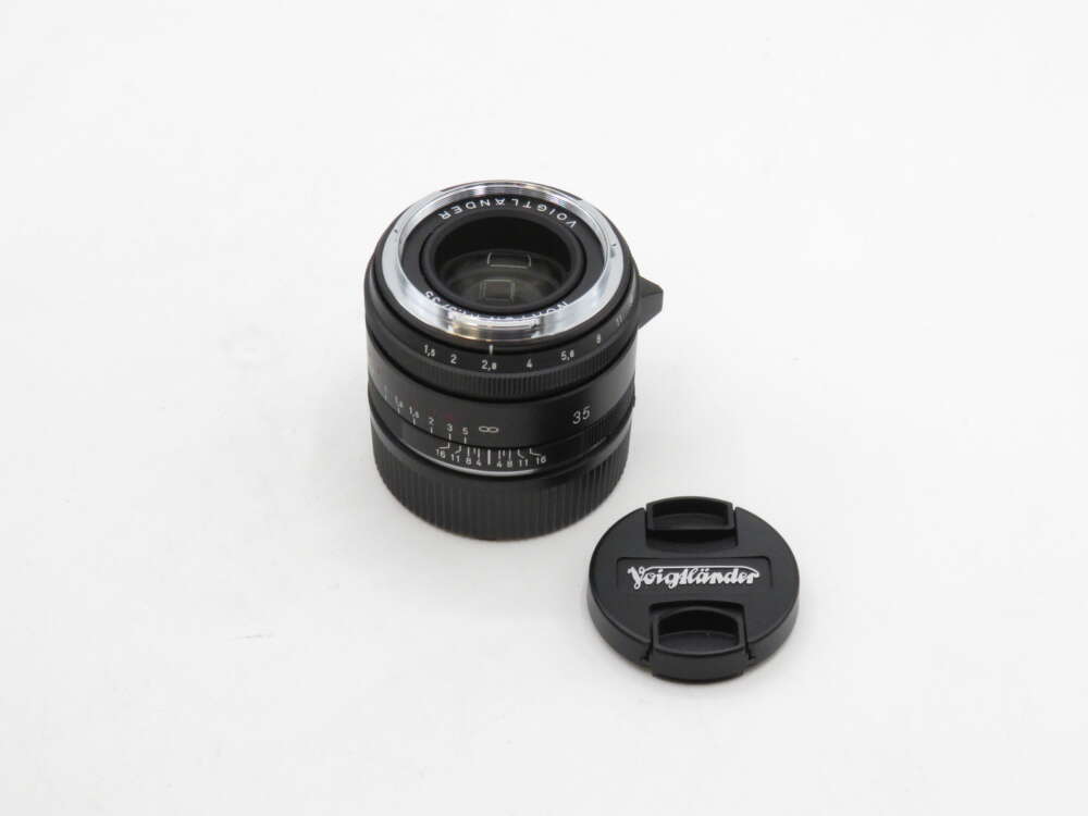 IMG_3494 A Voigtländer camera lens with a 35mm marking, accompanied by its lens cap on a plain white background.