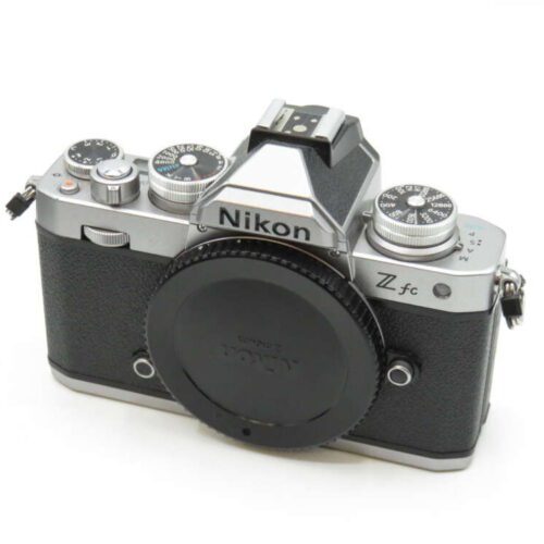 A Nikon Z fc camera with a vintage design and black textured grip, featuring multiple dials and a Sony lens cap.
