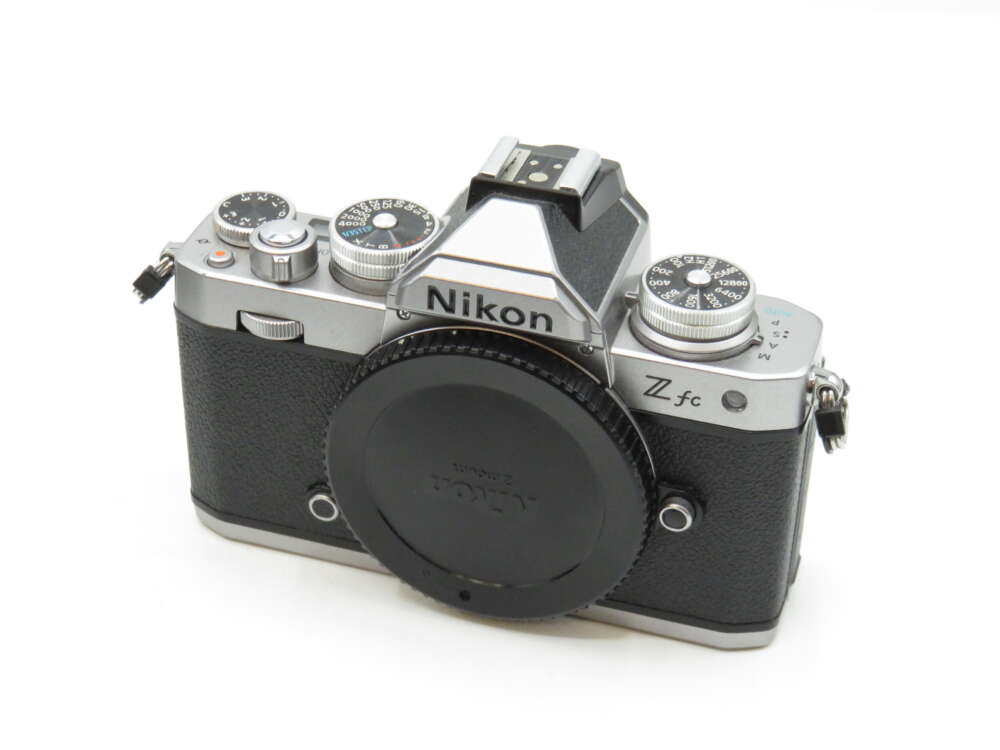 IMG_3503 A Nikon Z fc camera with a vintage design and black textured grip, featuring multiple dials and a Sony lens cap.