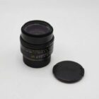 Camera lens with focus markings and detachable lens cap lying beside it.