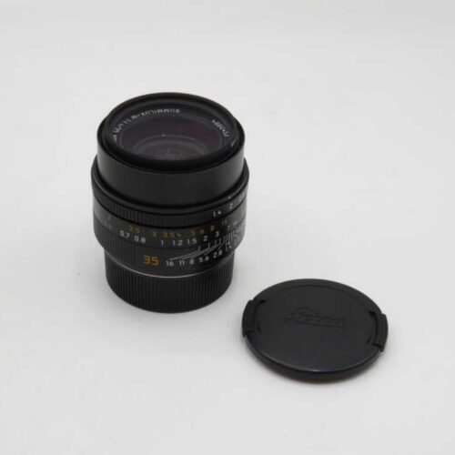 Camera lens with focus markings and detachable lens cap lying beside it.