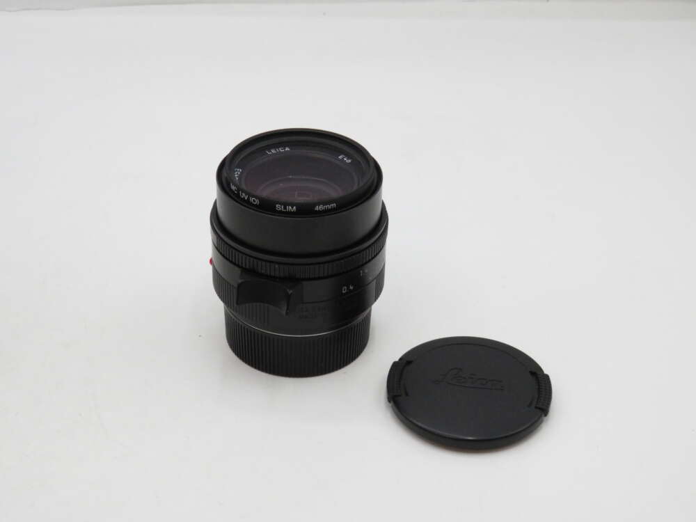 A Leica camera lens with its cap placed beside it on a plain white surface.